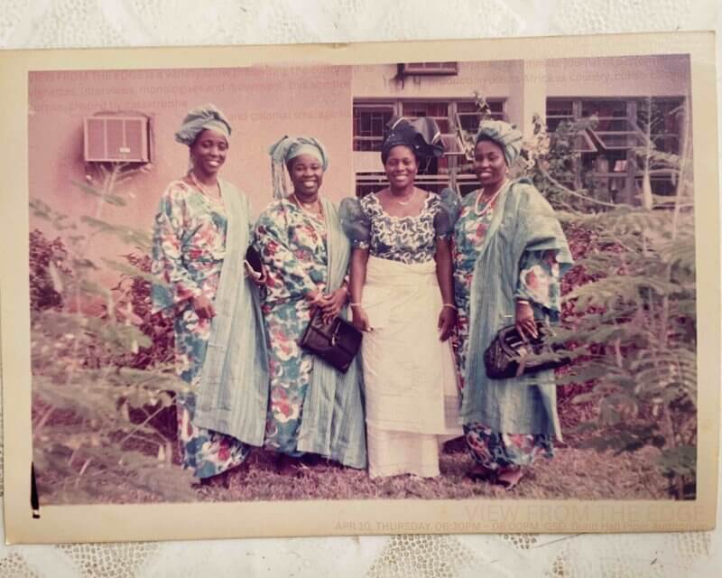 Old color photograph of 4 Nigerian women posing in coordinating traditional outfits
