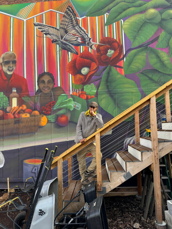 Kannan on stairs with colorful mural of people and produce behind him on shipping container.